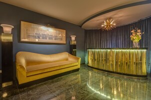 A reception area with a gold sofa, a framed cityscape artwork, a decorative light fixture, and a curtain backdrop.