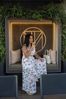 Una mujer sentada en un banco con un gran logotipo iluminado al fondo, rodeada de follaje.