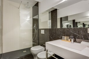A modern bathroom with a glass-enclosed shower, a white sink with toiletries, and a marble-tiled wall.