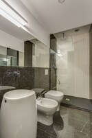 Une salle de bain moderne avec un lavabo en marbre, deux toilettes, un bidet et une douche séparée par une paroi de verre.