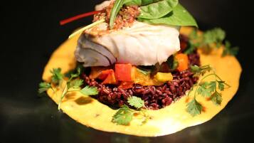 Un plat composé d’un morceau de poisson, de riz rouge et de légumes, le tout présenté dans une assiette.