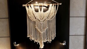 A bed with a macrame hanging light fixture above it, a patterned throw blanket, and a bedside table with a lamp and a vase. - Cors Hotel (Biguglia)