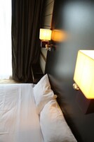 Una habitación de hotel con una cama bien hecha, cortinas oscuras y lámparas fijadas a la pared.