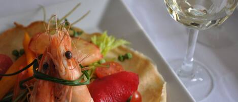 A plate of food with shrimp and vegetables, a glass of white wine, and a white tablecloth.