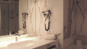 Une salle de bain avec un meuble-lavabo en marbre, un sèche-cheveux fixé au mur et un porte-serviettes.