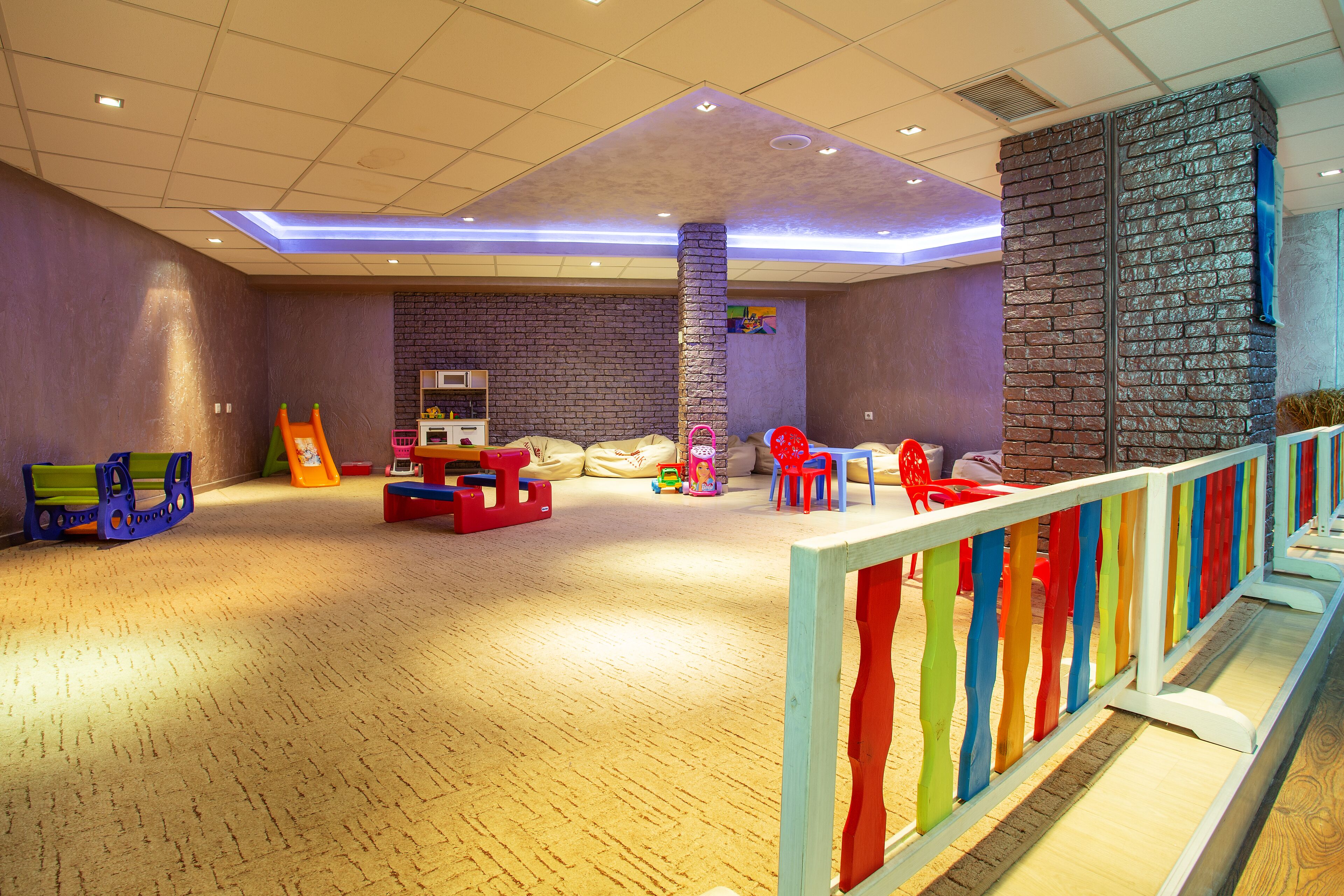 A children's play area with a brick wall, wooden flooring, and colorful play equipment.