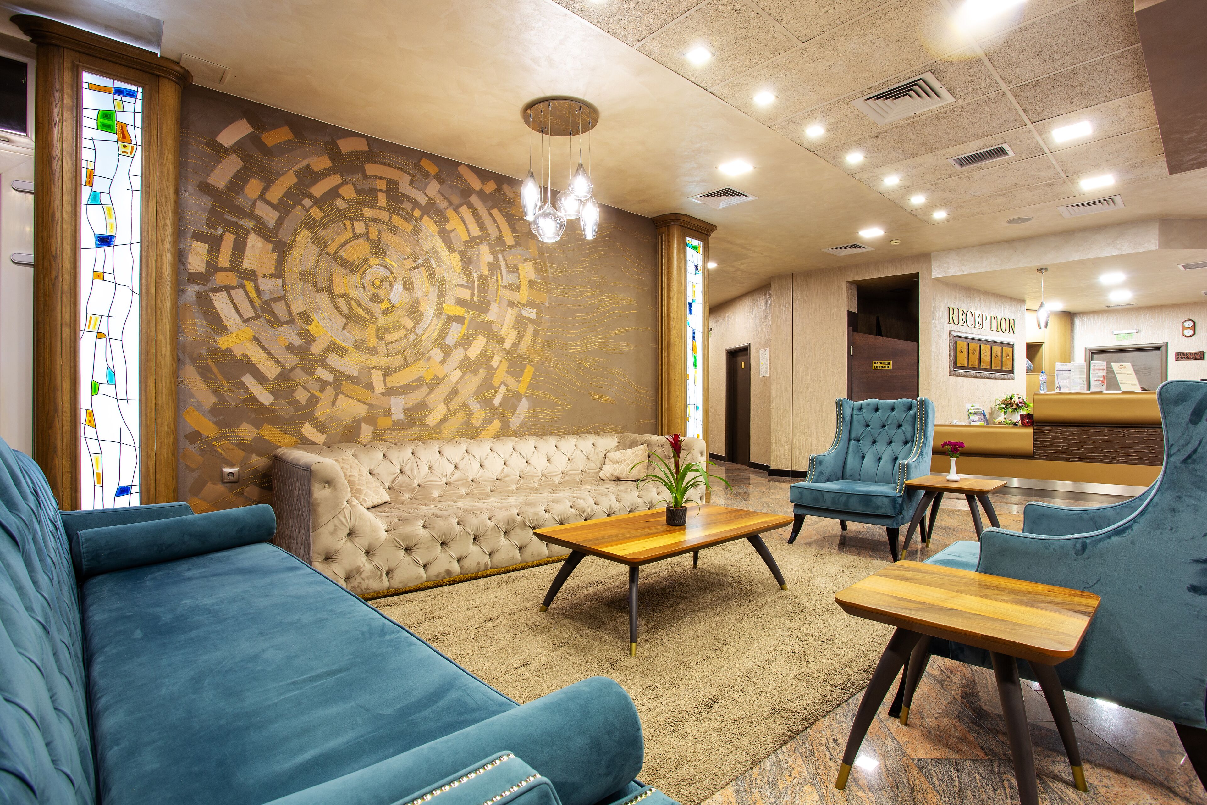 Un vestíbulo con un sofá capitonado, sillones azules, una mesa de centro de madera y un mostrador de recepción.