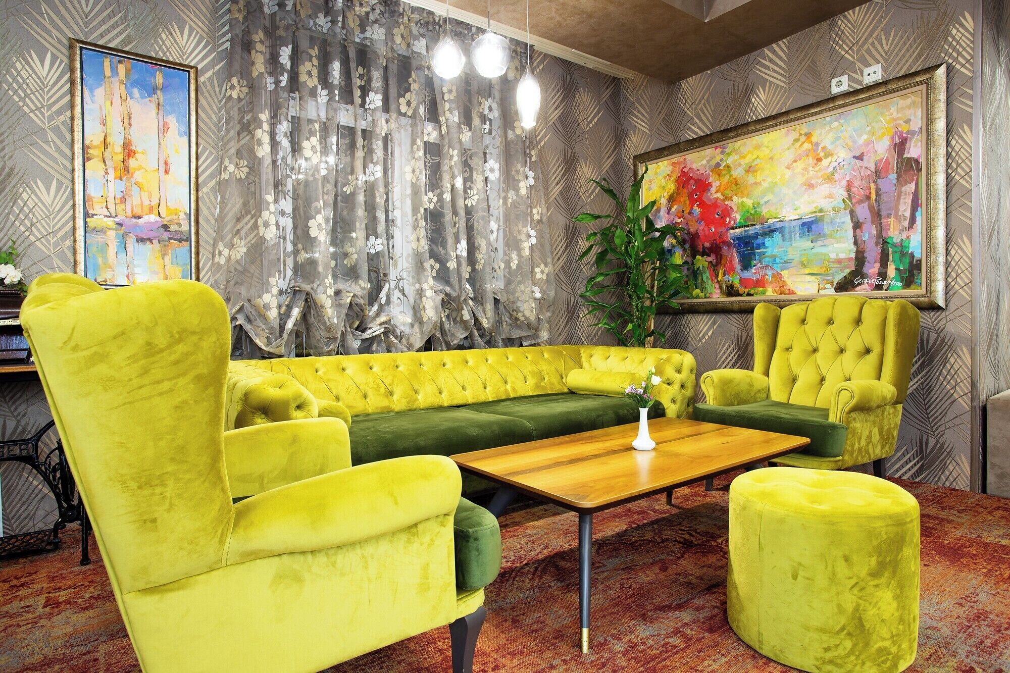 Ein Zimmer mit gelbem Sofa, einem grünen Akzentsofa, einem Holztisch und einem großen Gemälde an der Wand.