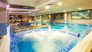 Een binnenzwembad met een jacuzzi, betegelde muren en grote ramen.
