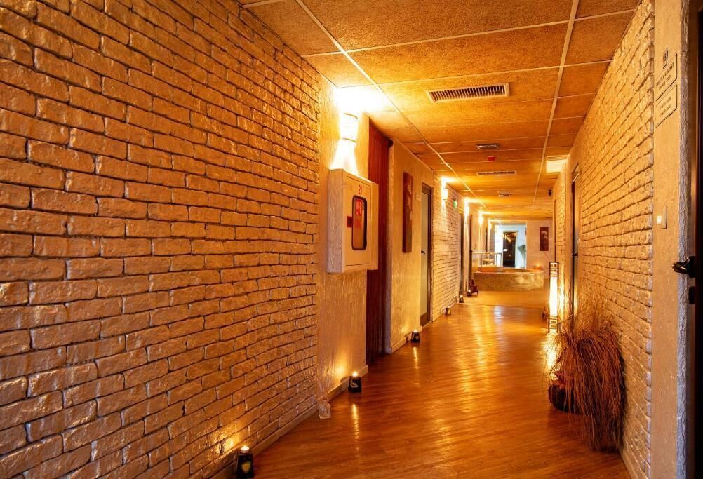 A corridor with brick walls and wooden flooring, leading to a room with a bed and a nightstand.
