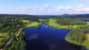 A golf course with a lake, surrounded by forested hills and a clear sky. - Isaberg Golfklubb (Hestra)