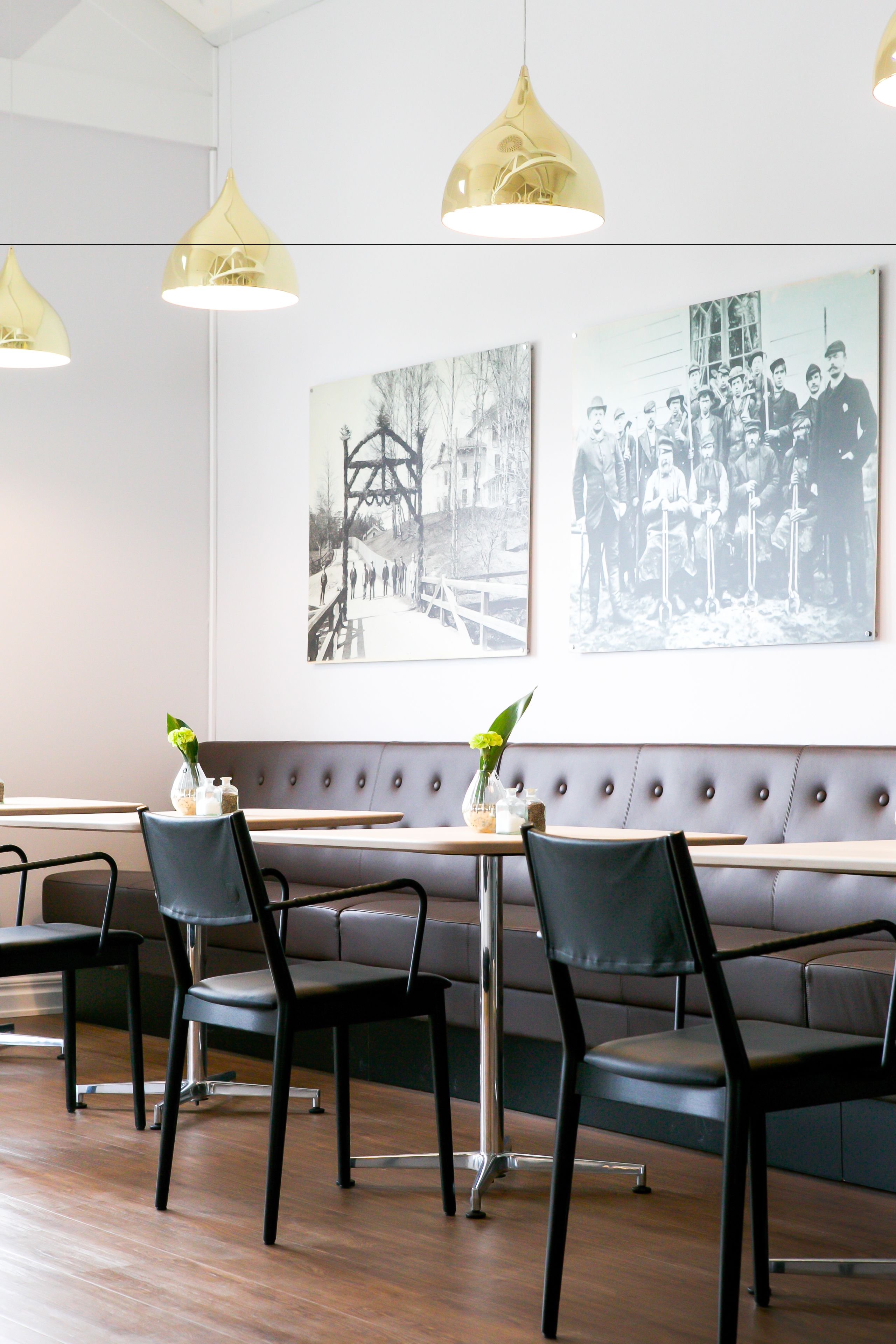 A modern restaurant interior with a long bench seating area, black chairs, and yellow pendant lighting.