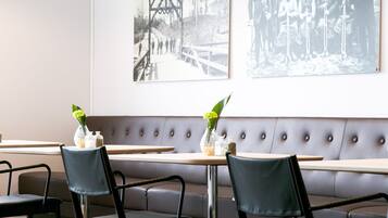 A modern restaurant interior with a long bench seating area, black chairs, and yellow pendant lighting.