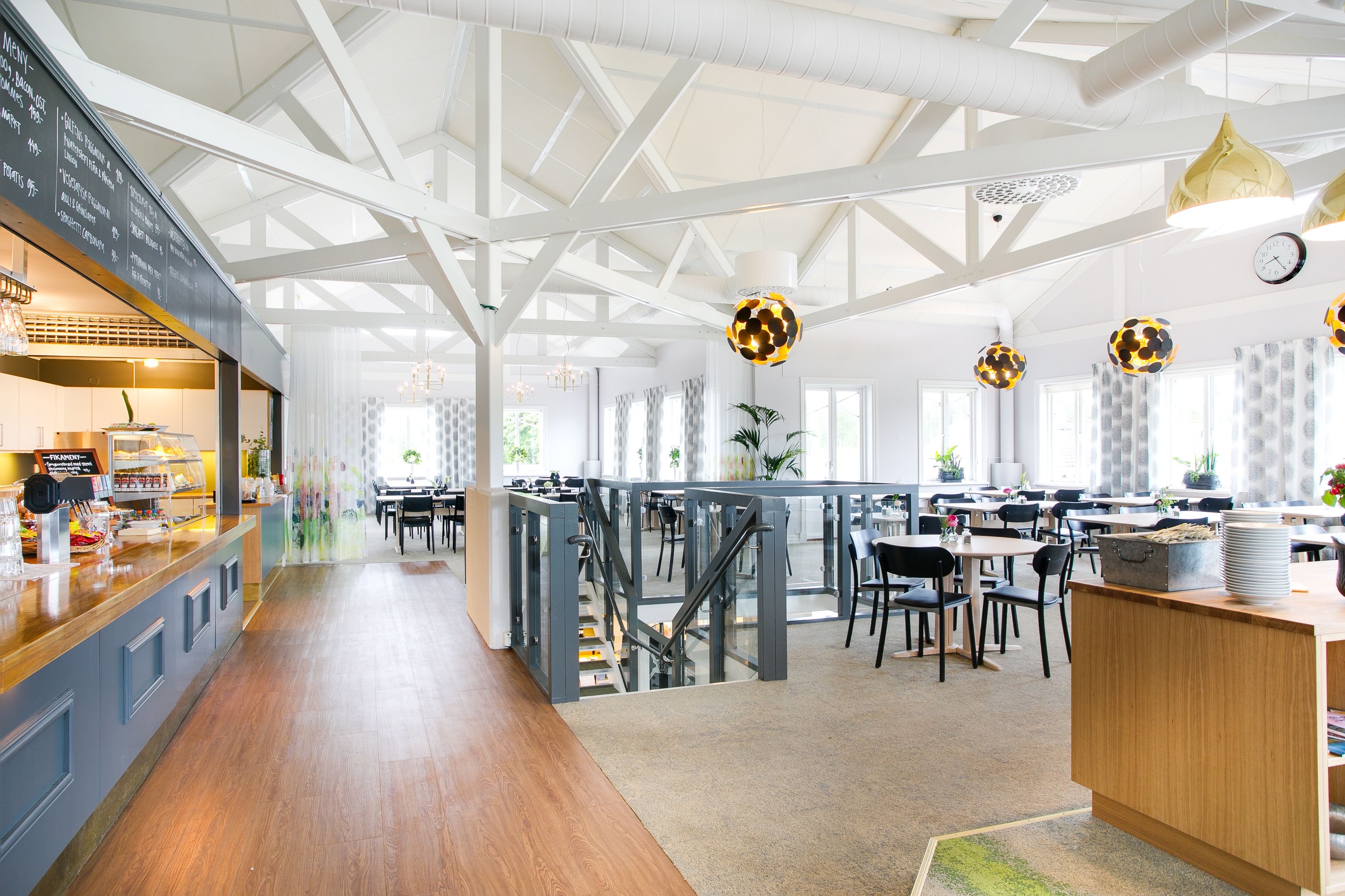 Une cafétéria spacieuse avec de hauts plafonds, des planchers en bois et un éclairage moderne suspendu.