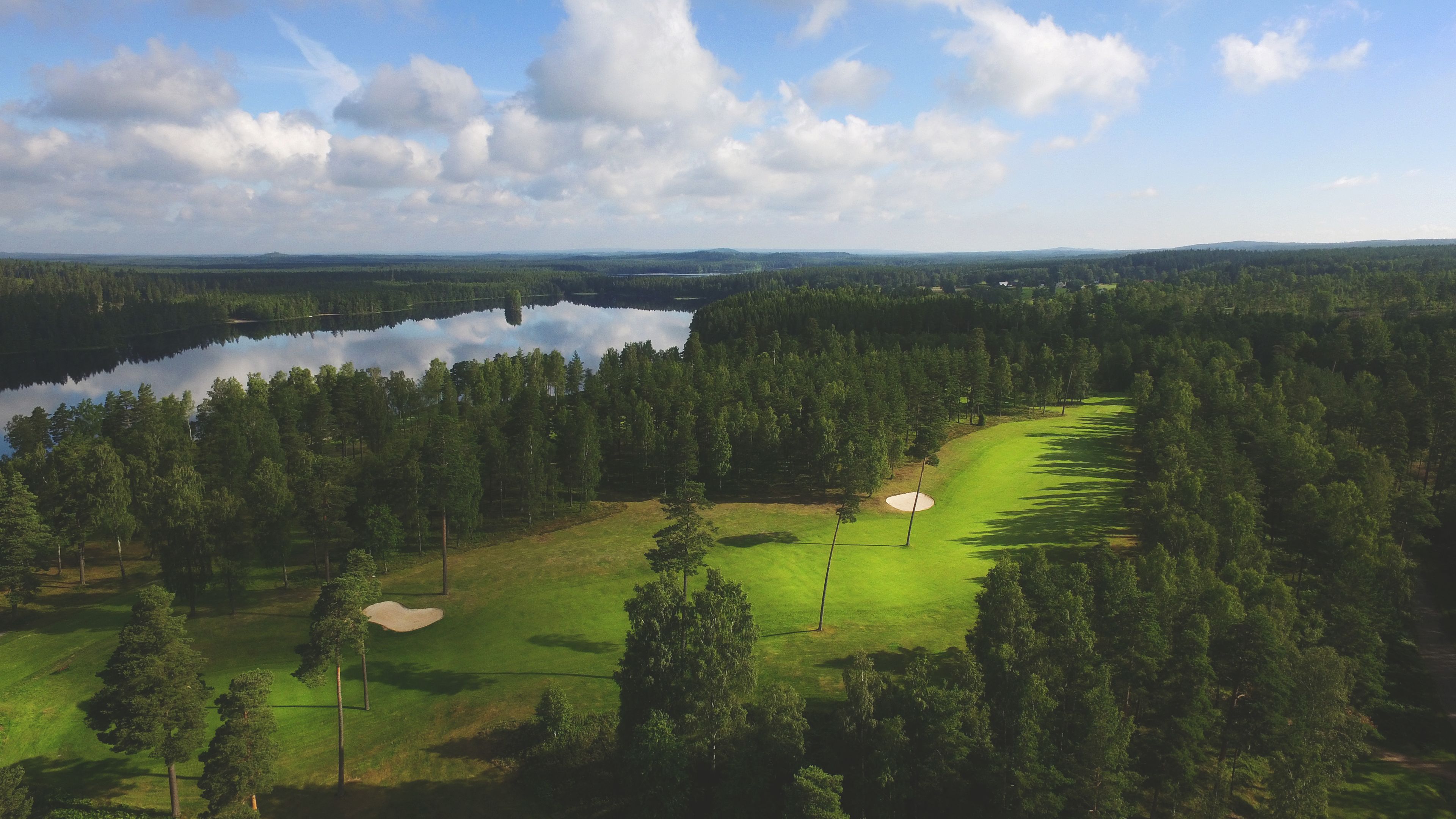 Camp de golf amb un cos d'aigua, envoltat per un bosc dens.