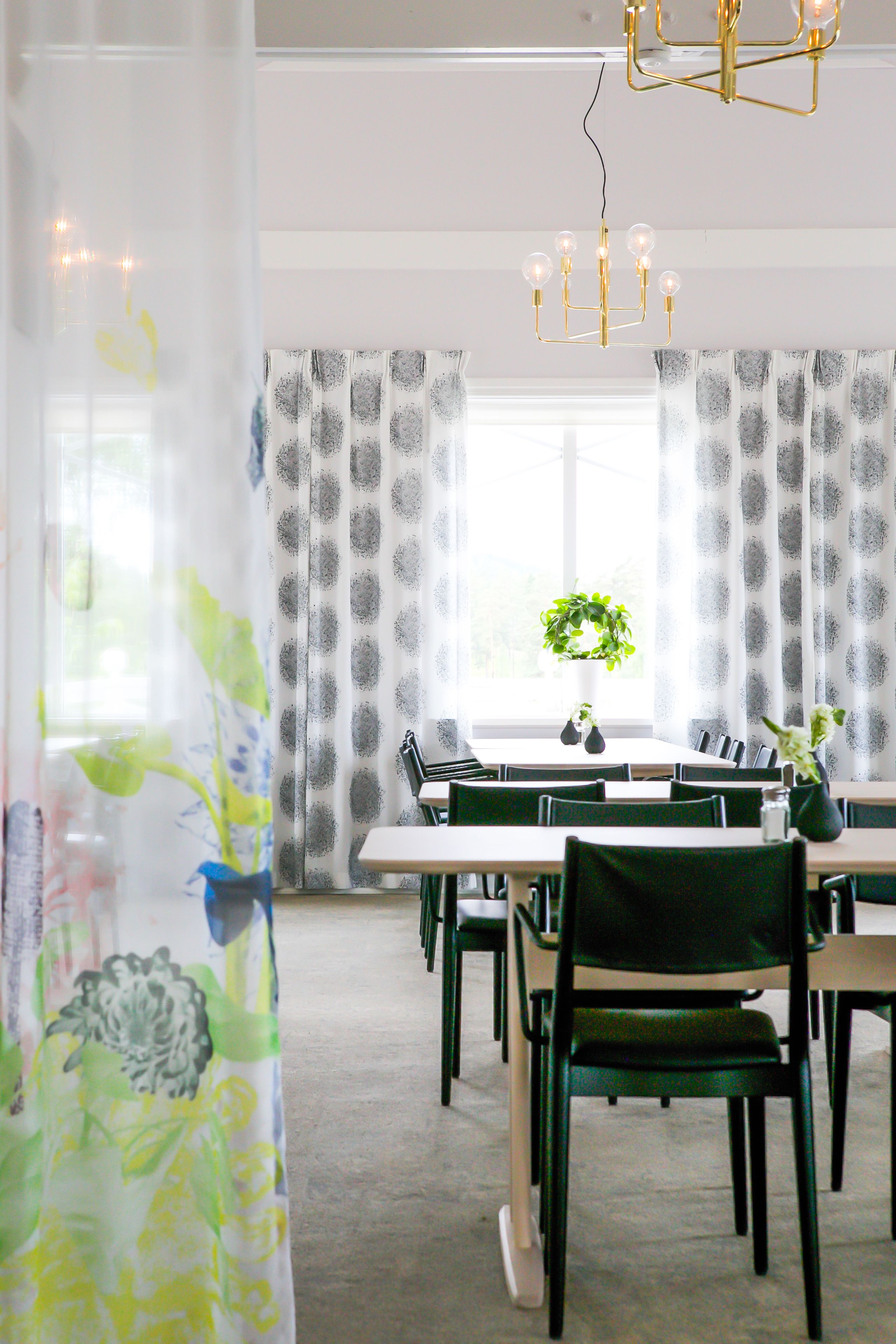 A dining area with a chandelier, patterned curtains, and a potted plant on the table.