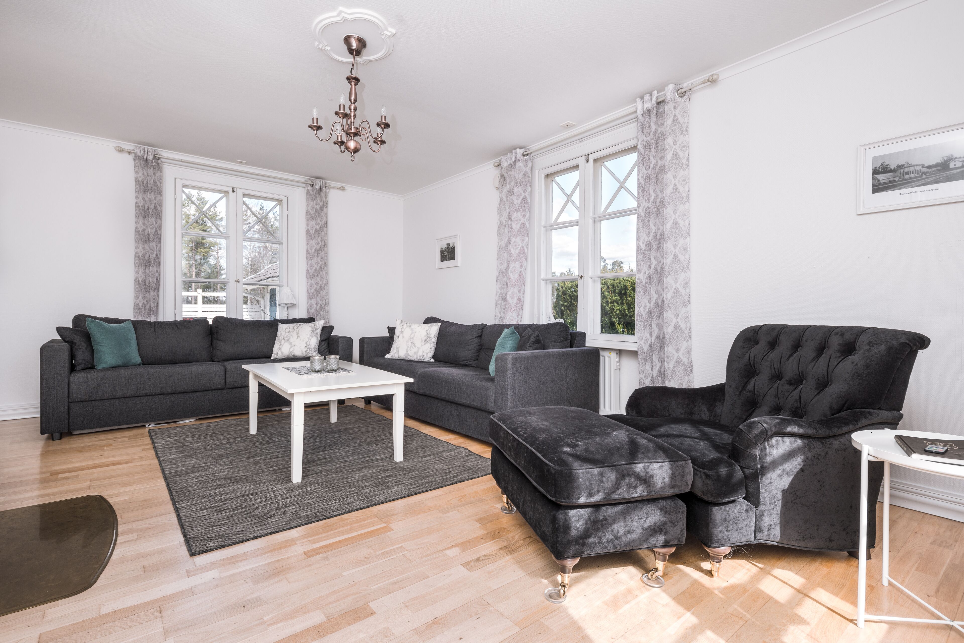 Una sala de estar moderna con un sofá seccional gris, un sillón de terciopelo negro y una mesa de centro blanca.