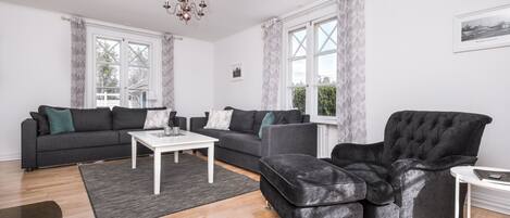 Una sala de estar moderna con un sofá seccional gris, un sillón de terciopelo negro y una mesa de centro blanca.