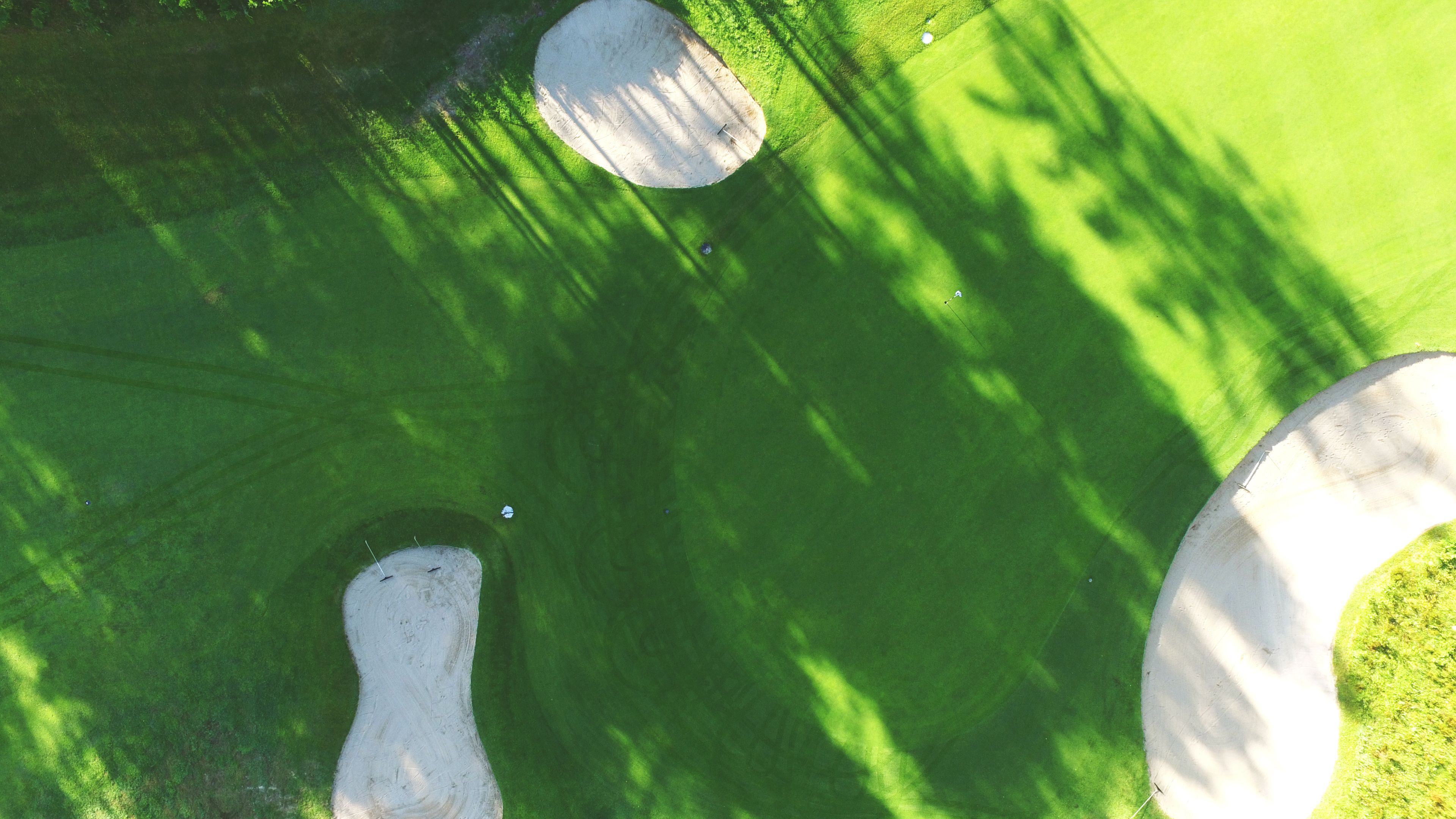 An aerial view of a golf course with three holes, surrounded by green grass and trees.
