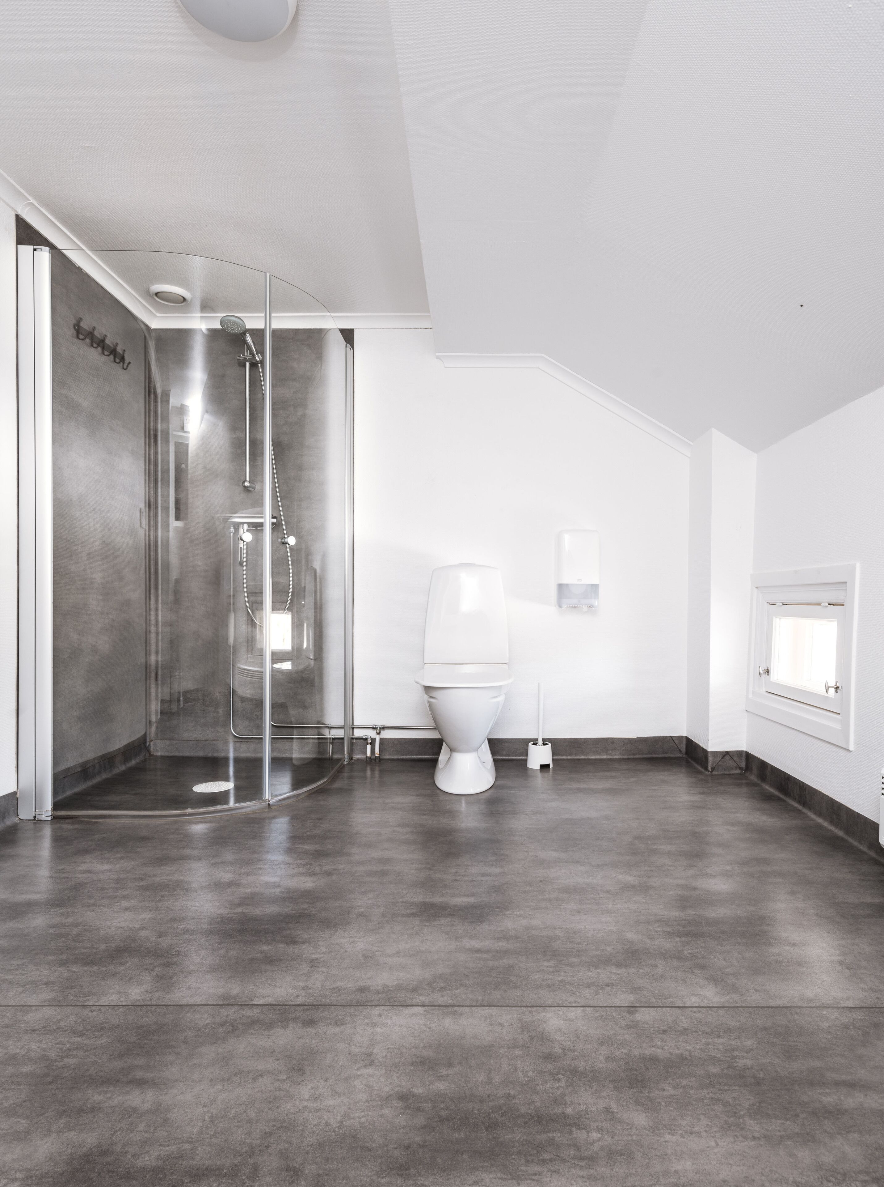 Een moderne badkamer met een douchecabine van glas, een wit toilet en een klein raam.