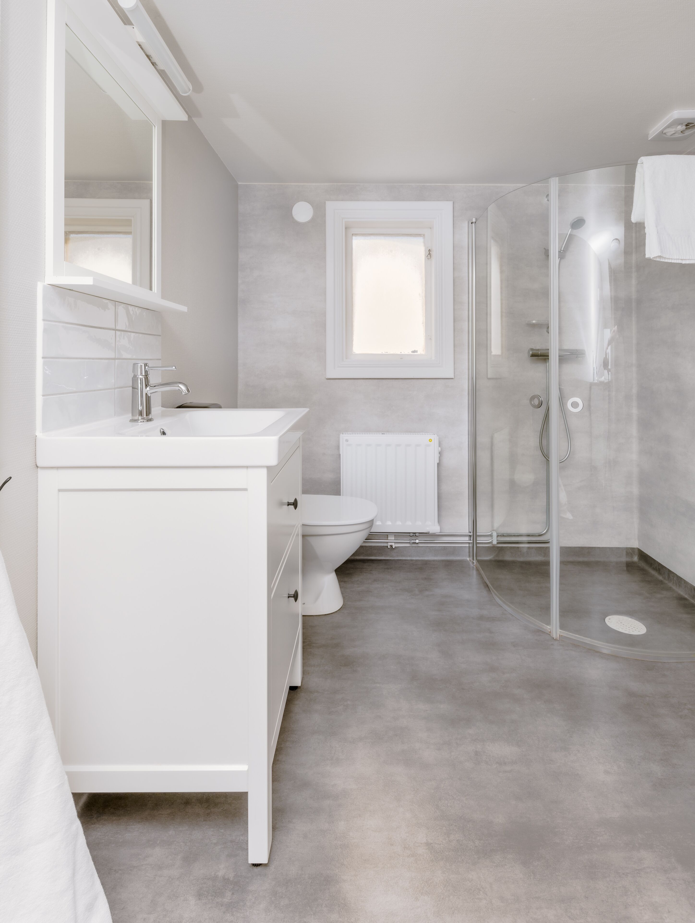 A modern bathroom with a white vanity, a toilet, a glass shower enclosure, and a window providing natural light.