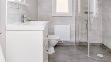 A modern bathroom with a white vanity, a toilet, a glass shower enclosure, and a window providing natural light.