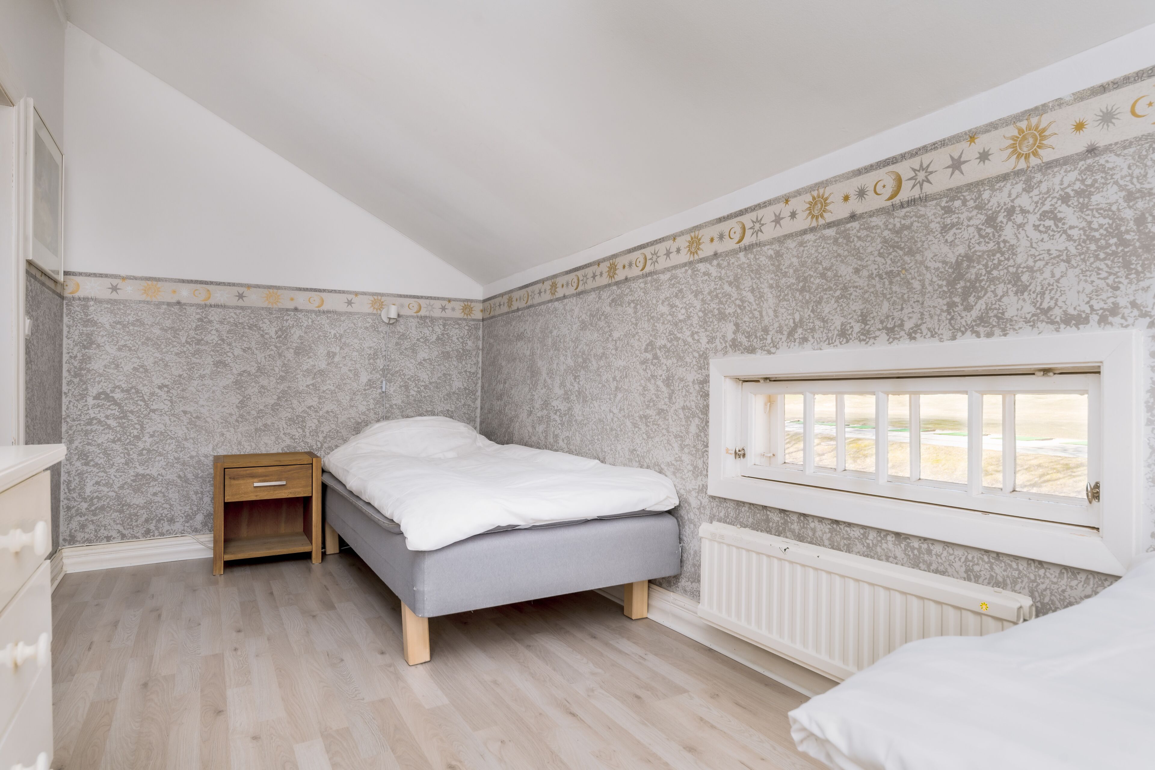 A bedroom with a bed, a nightstand, a window with a view, and a radiator.