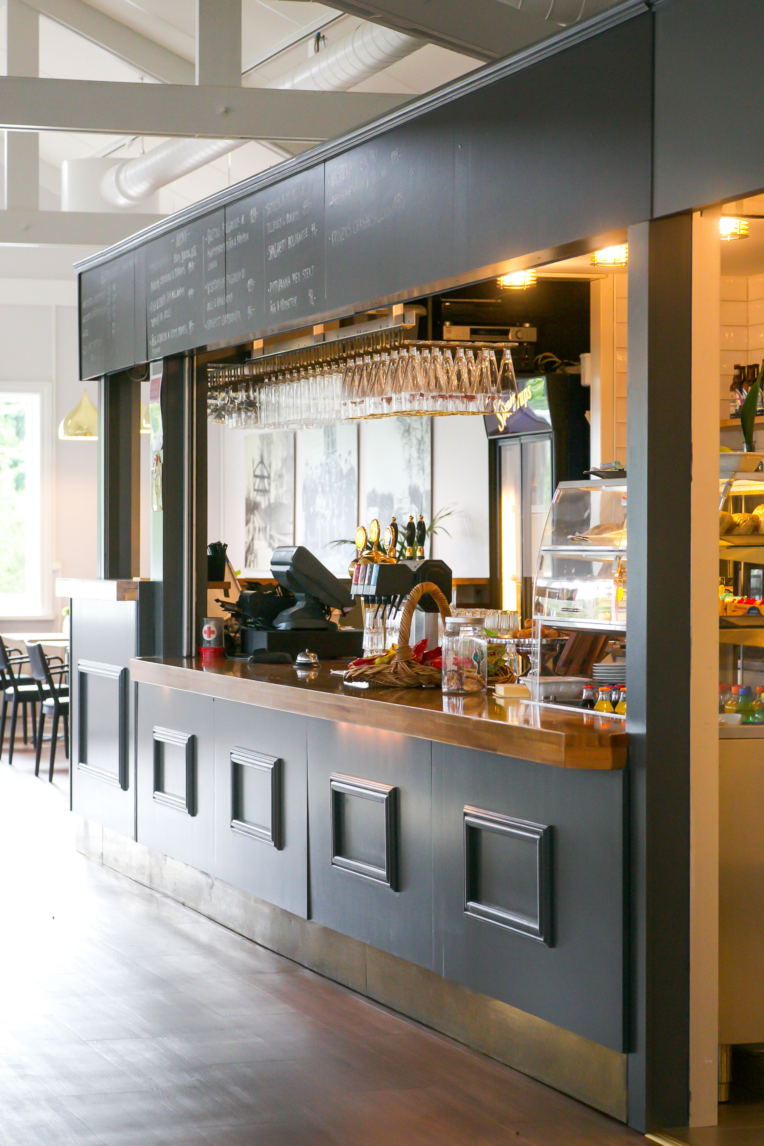 Un espace bar moderne avec un tableau noir servant de menu, des verres à vin et une machine à café.