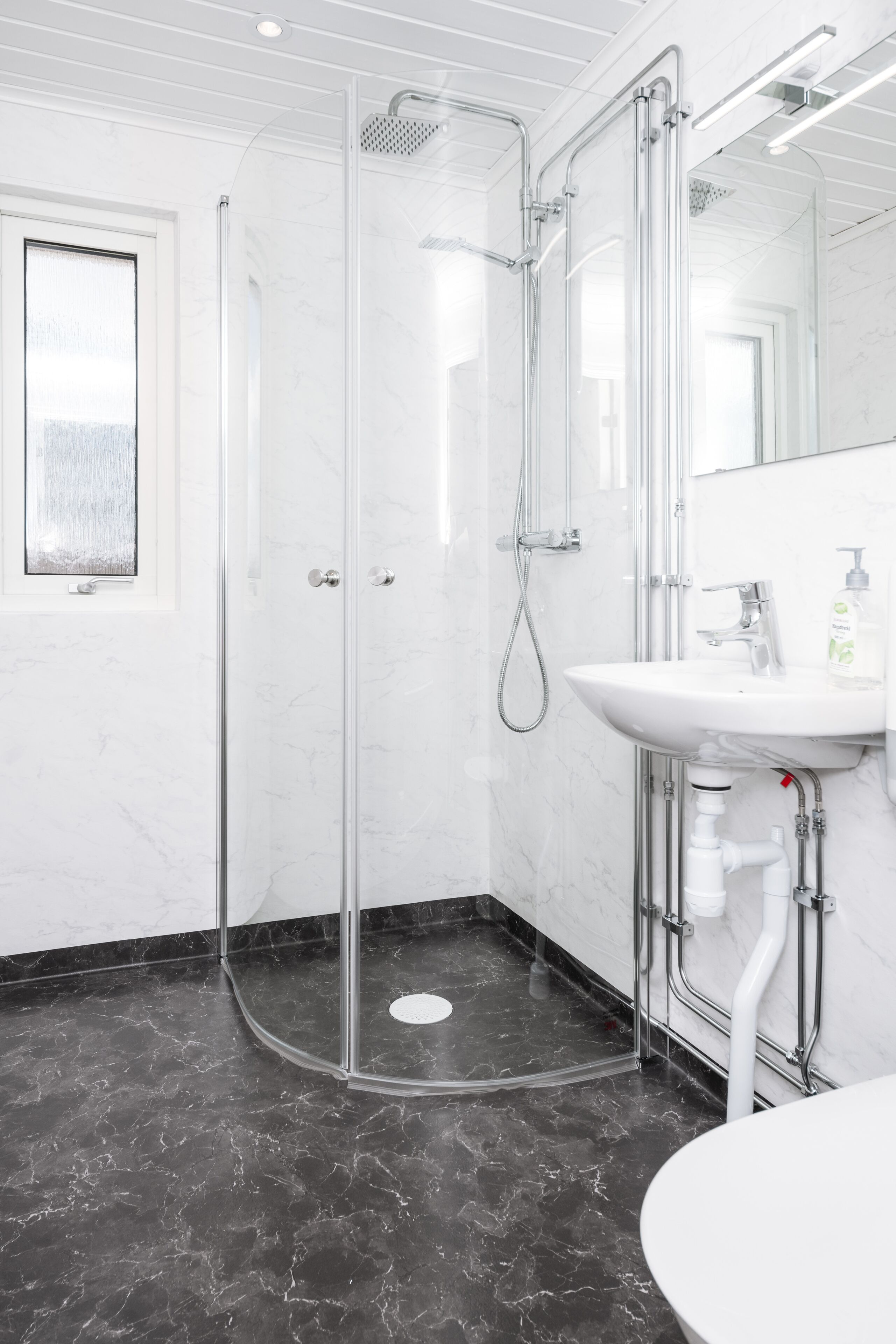 A modern bathroom with a glass-enclosed shower, a white sink, and a marble floor.