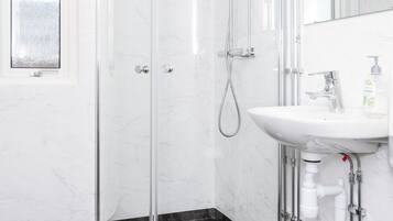A modern bathroom with a glass-enclosed shower, a white sink, and a marble floor.