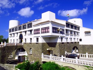 A multi-story building with a white facade, stone base, and balconies. - Penghu Youth Activity Center (Magong)