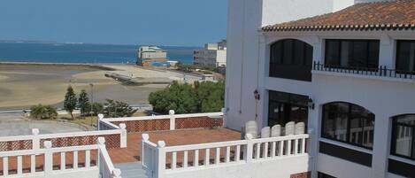 Un edificio blanco con una torre, un patio con plantas en macetas y vista al mar.
