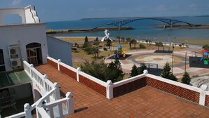 Une terrasse sur le toit offrant une vue sur un pont bleu enjambant une étendue d’eau, une aire de jeux et un bâtiment blanc doté de climatiseurs.