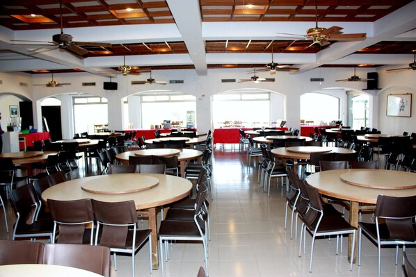 A spacious dining area with multiple round tables and chairs, ceiling fans, and large windows allowing natural light. - Penghu Youth Activity Center (Magong)