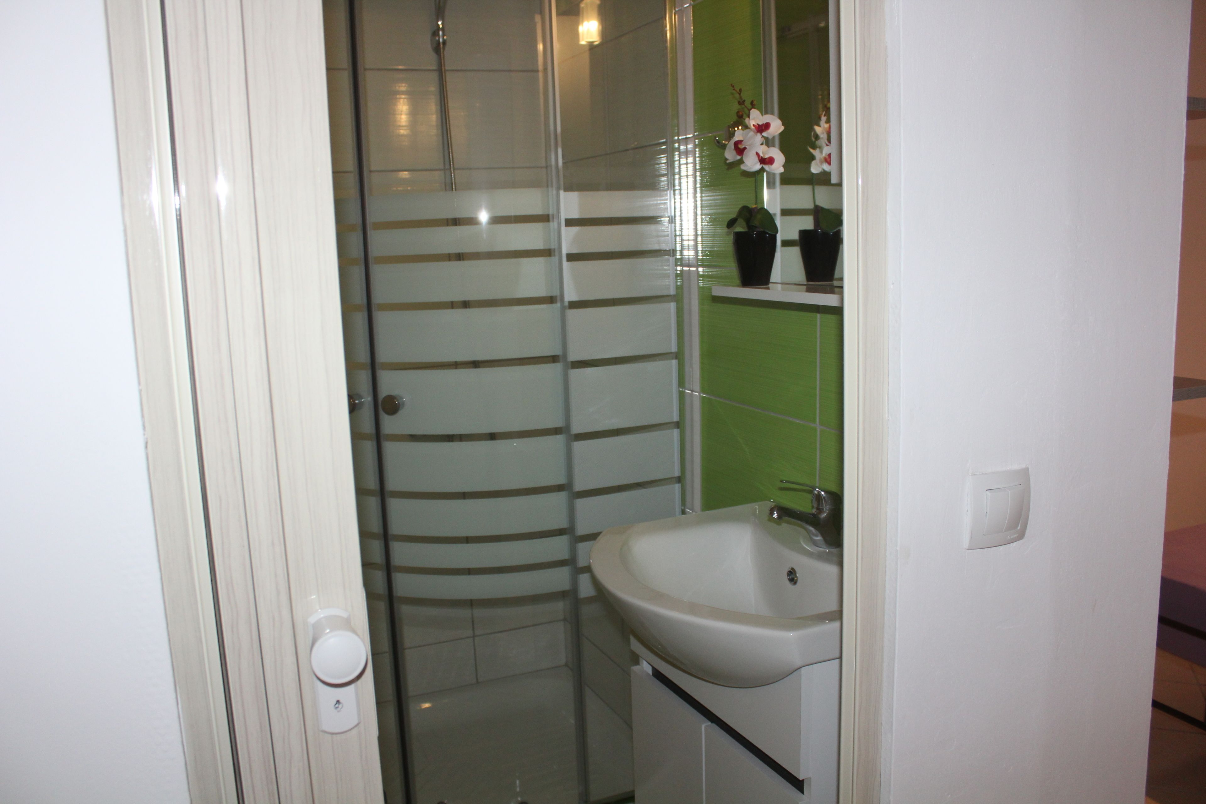 Un bagno con box doccia in vetro, lavandino bianco e parete rivestita in piastrelle verdi.