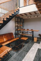 Een modern interieur met een trap, een houten bank, een bankstel, een eettafel met stoelen en een ventilator.
