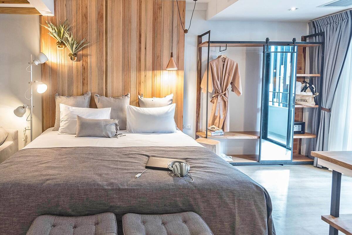 A modern bedroom with a large bed, bedside lamps, a sofa, and a clothing rack.