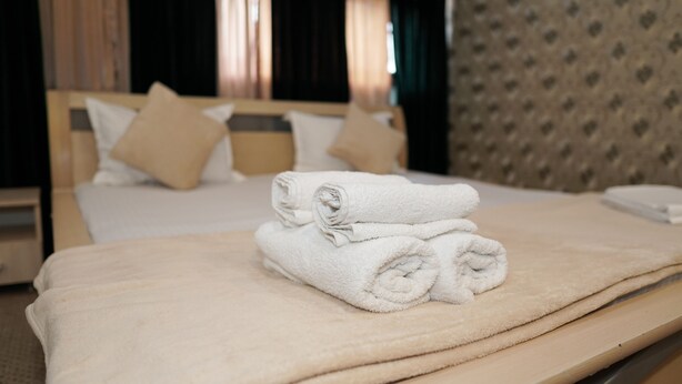 Una cama bien hecha con toallas blancas, un cabecero de madera y ropa de cama color beige en una habitación de hotel.