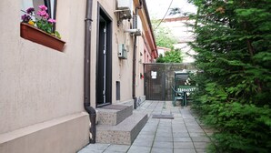 Un estrecho callejón con una pequeña zona de estar al aire libre, escalones que llevan a una puerta y un jardín con helechos.