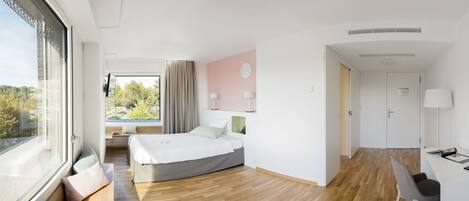 Una habitación de hotel moderna con un ventanal grande, una cama, un escritorio y una silla.