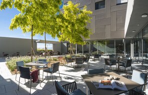 An outdoor seating area with tables and chairs, surrounded by glass walls and a building with a modern design. - Hôtel des Patients (Lausanne)