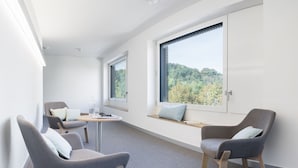 A modern room with two grey chairs, a small round table, and a window with a view of trees. - Hôtel des Patients (Lausanne)
