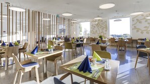 A modern dining area with multiple tables and chairs, large windows, and a ceiling with circular light fixtures. - Hôtel des Patients (Lausanne)