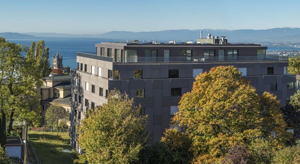 Un edificio moderno con terraza en la azotea, rodeado de árboles y vistas al mar y a las montañas.