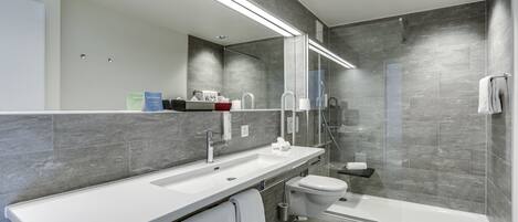 A modern bathroom with a large mirror, white sink, and a walk-in shower.