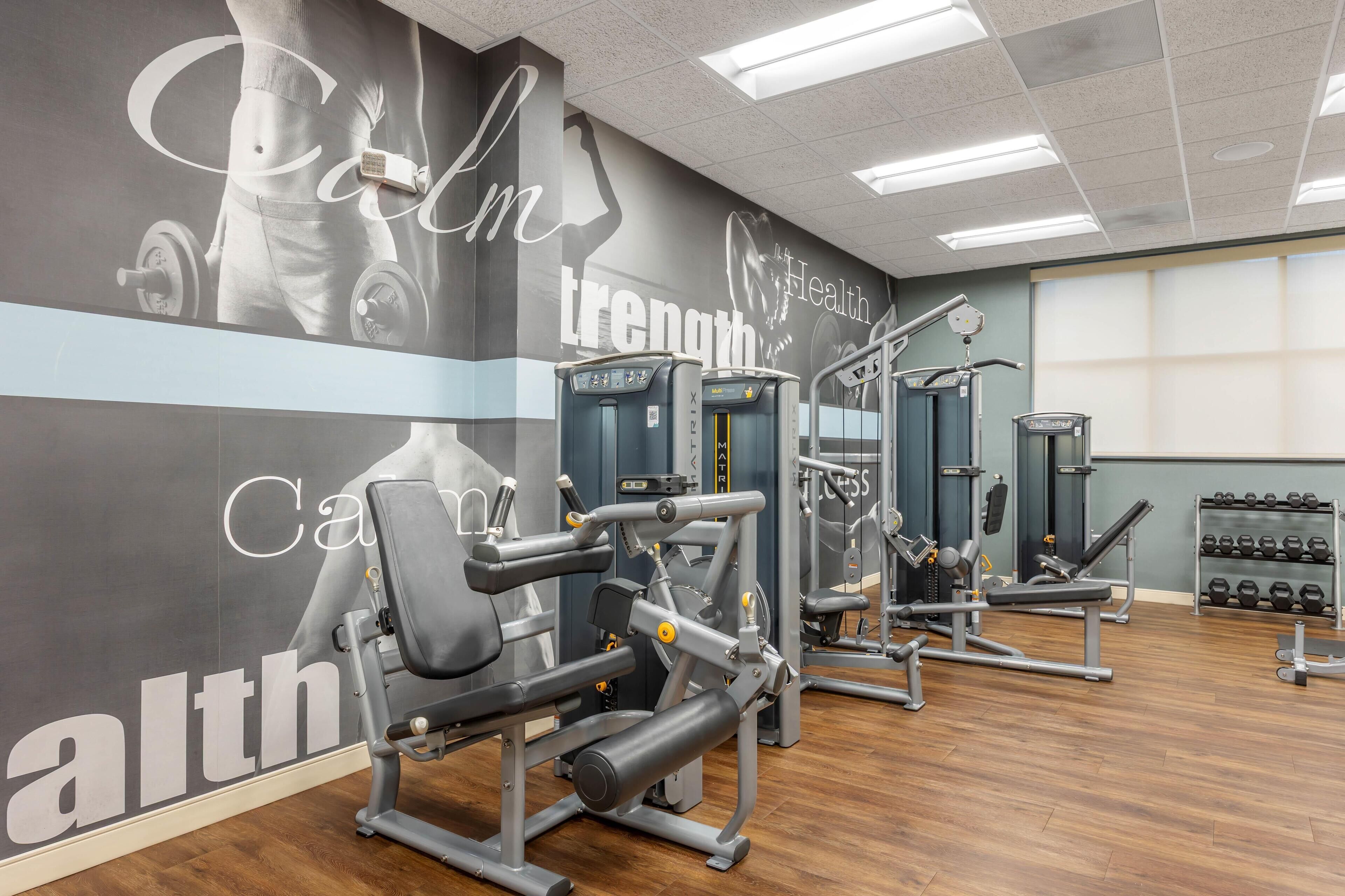 A gym with weight machines, dumbbells, and a motivational wall.