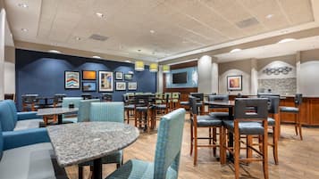 Un restaurant avec des banquettes, des tables et des chaises, dont les murs sont ornés d’œuvres d’art et qui est équipé d’un téléviseur à écran plat.