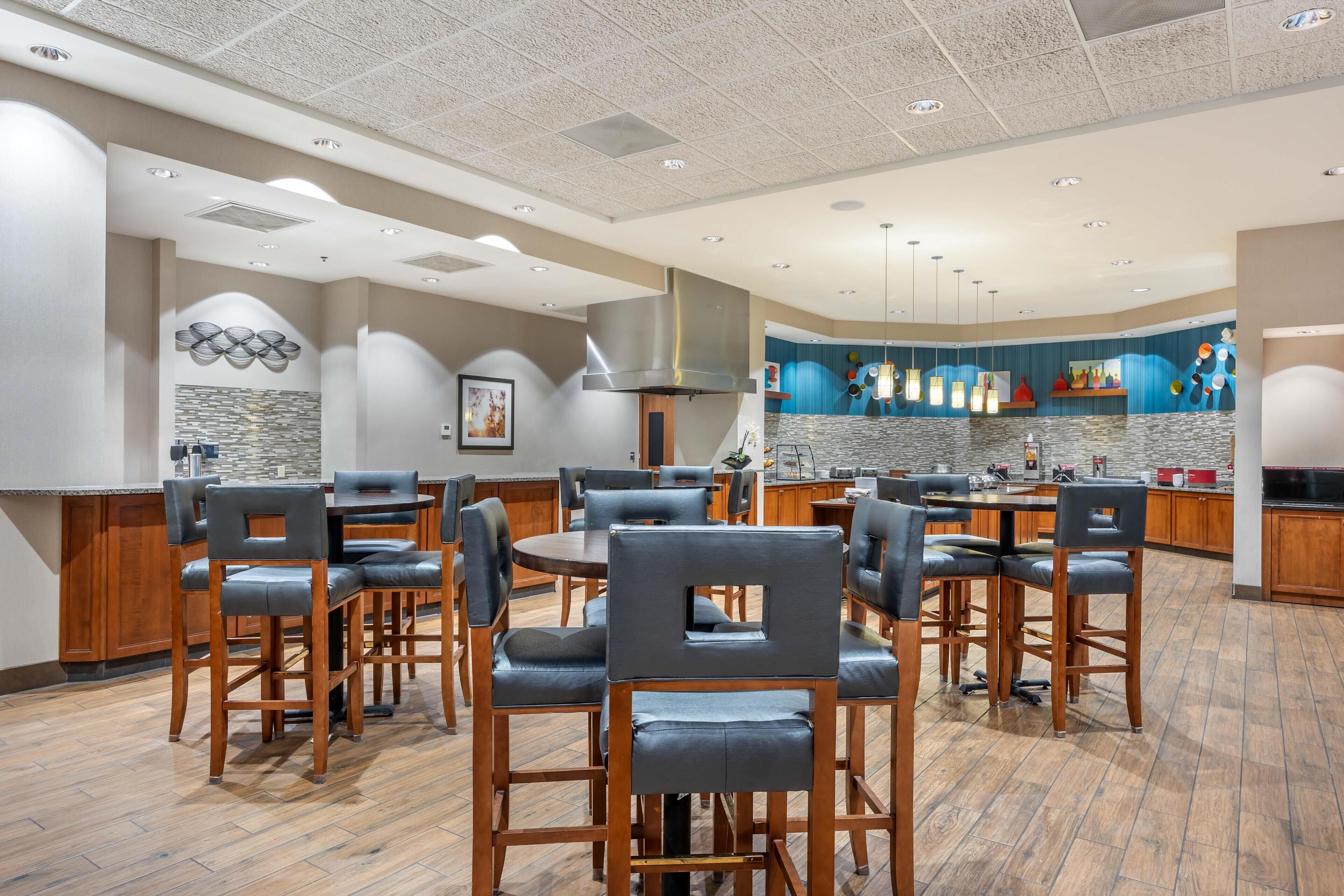 A spacious dining area with multiple tables and chairs, a kitchen area with modern appliances, and a decorative wall with a geometric pattern.
