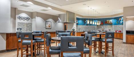 A spacious dining area with multiple tables and chairs, a kitchen area with modern appliances, and a decorative wall with a geometric pattern.