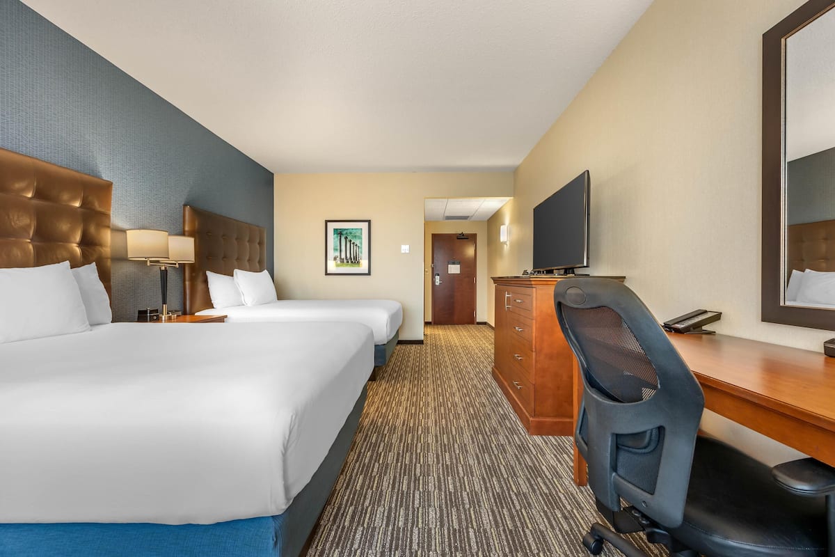 A hotel room with two beds, a desk, a chair, a television, and a door leading to another room.